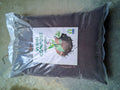 A large clear plastic bag filled with dark brown vermi compost manure, featuring a white label with green and black text and a small green leaf logo, placed on a concrete floor.